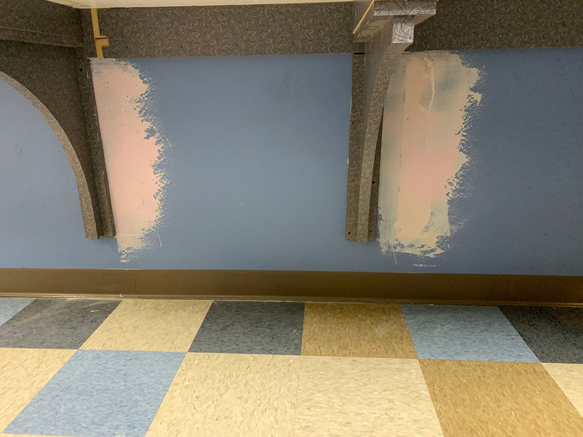 A blue wall is being painted in a room with a checkered floor.