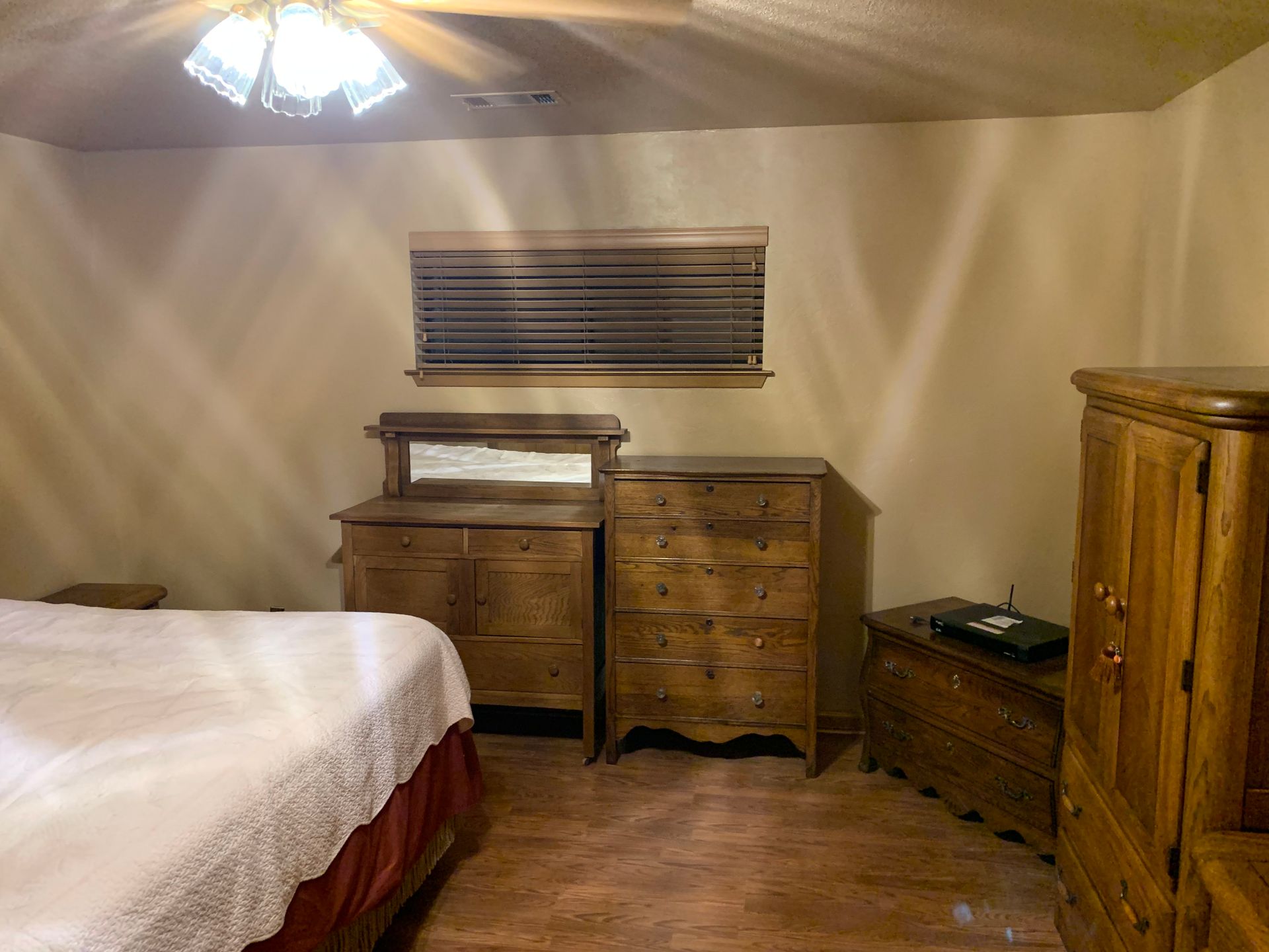 A bedroom with a bed , dresser , chest of drawers and a window.