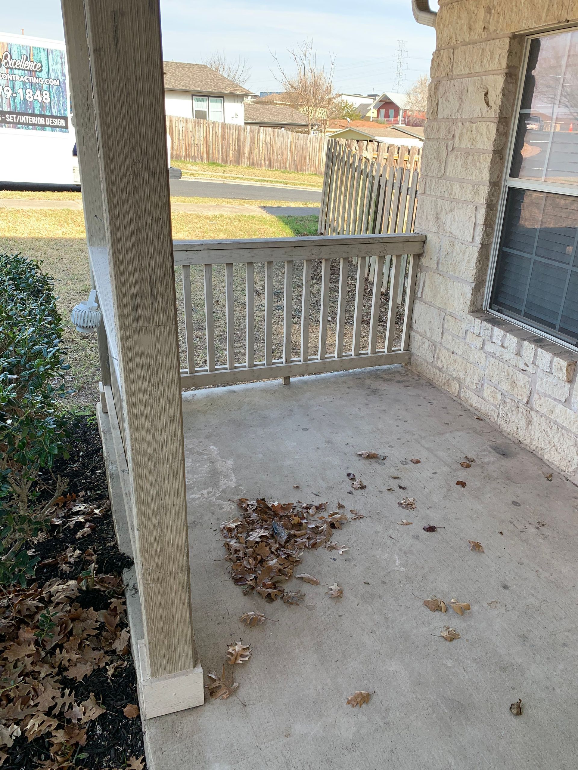An empty porch with a railing and leaves on the ground.