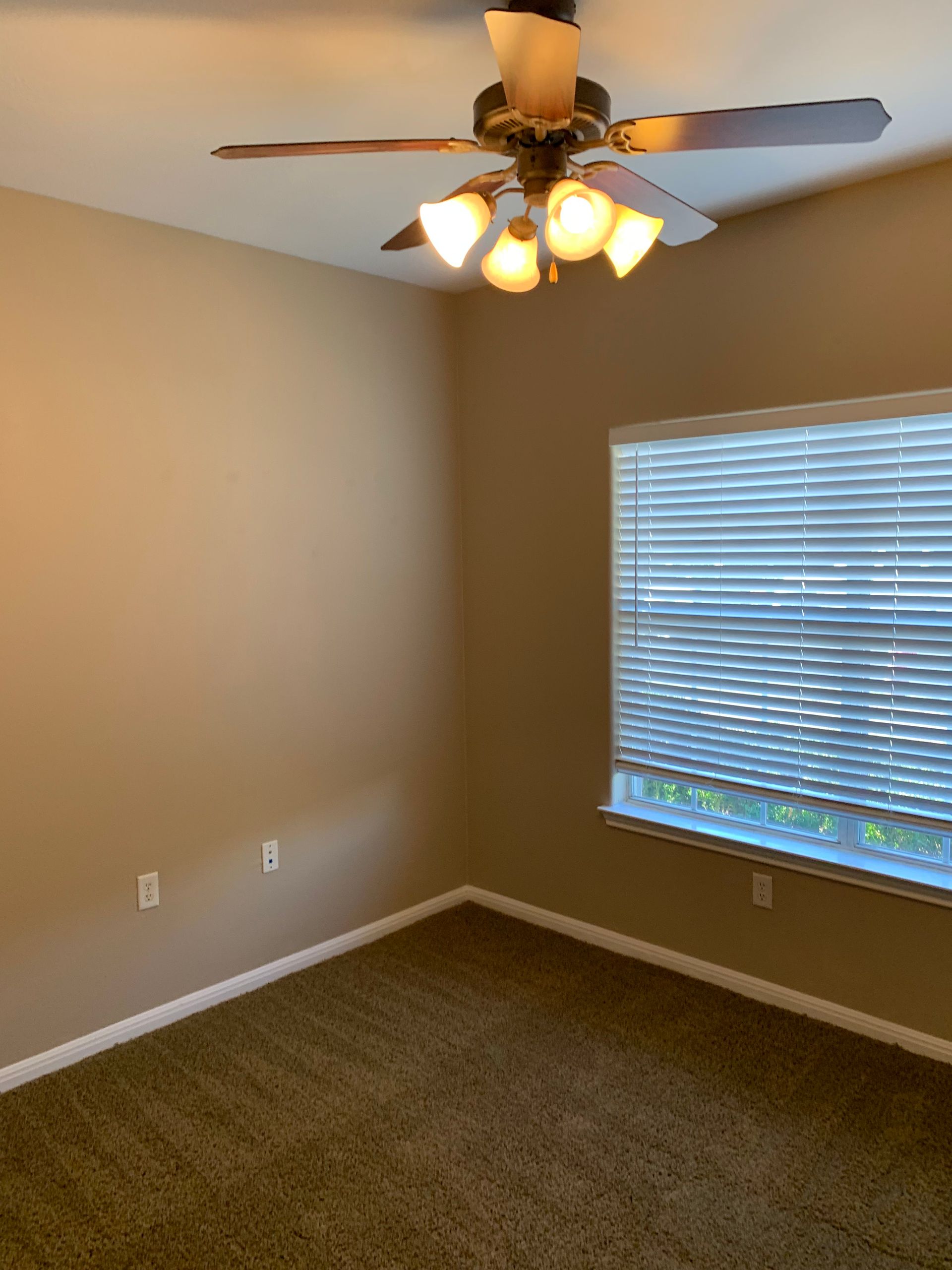 An empty bedroom with a ceiling fan and a window.