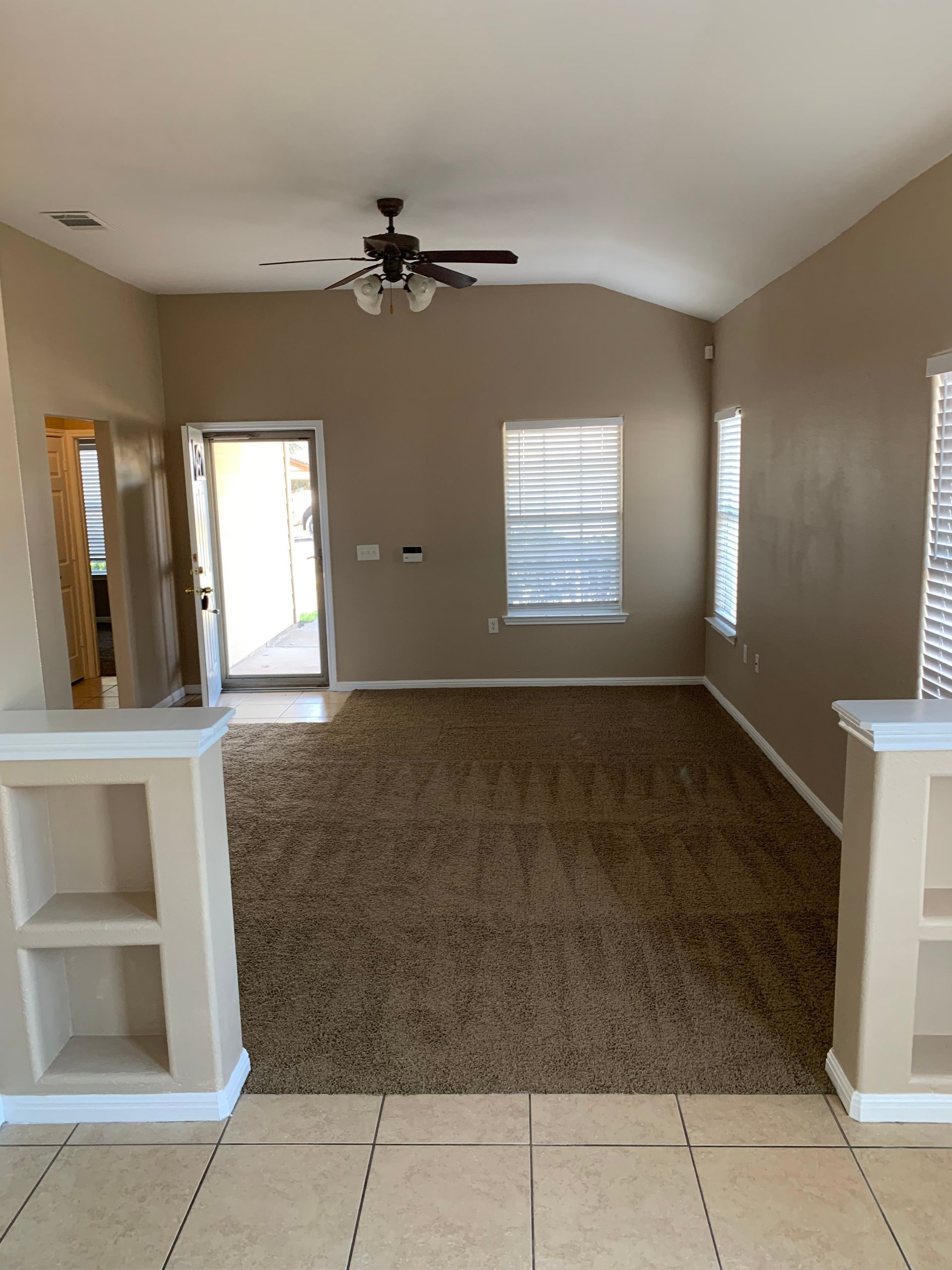 An empty living room with a ceiling fan and a window.