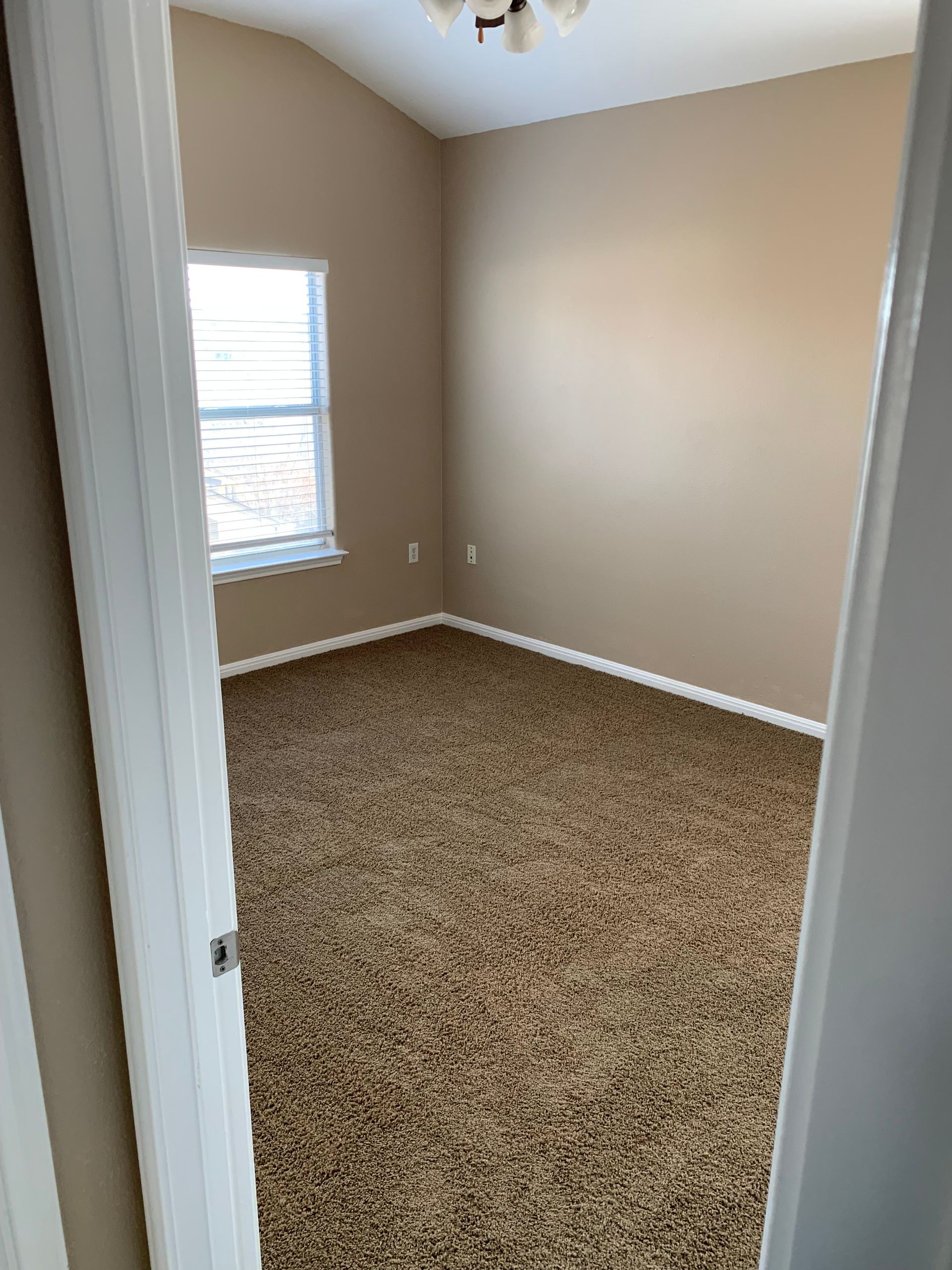 An empty bedroom with a carpeted floor and a window.