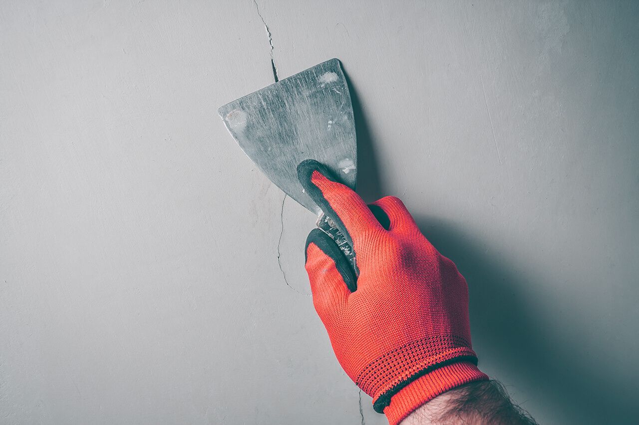 A person wearing red gloves is holding a spatula and plastering a wall.