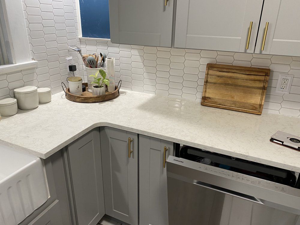 A kitchen with white cabinets , a stainless steel dishwasher and a wooden cutting board on the counter.