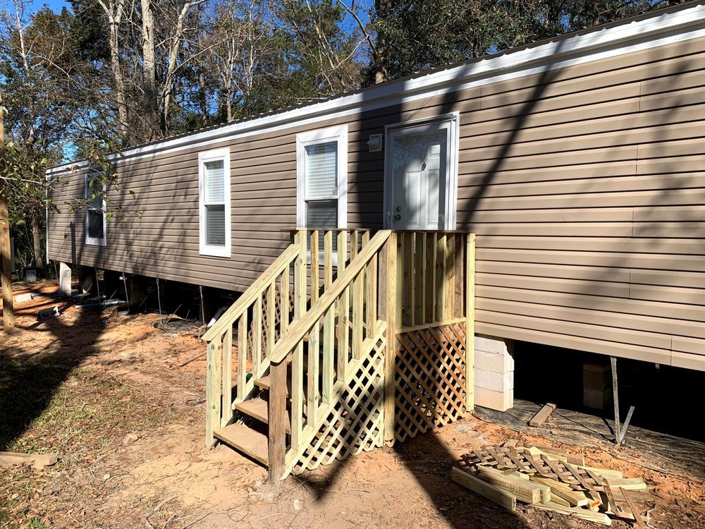A mobile home with a wooden deck and stairs.