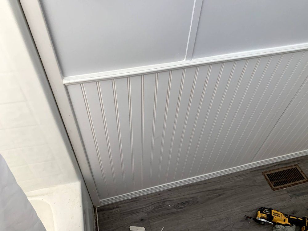 A ceiling with white paneling and a drill on the floor.