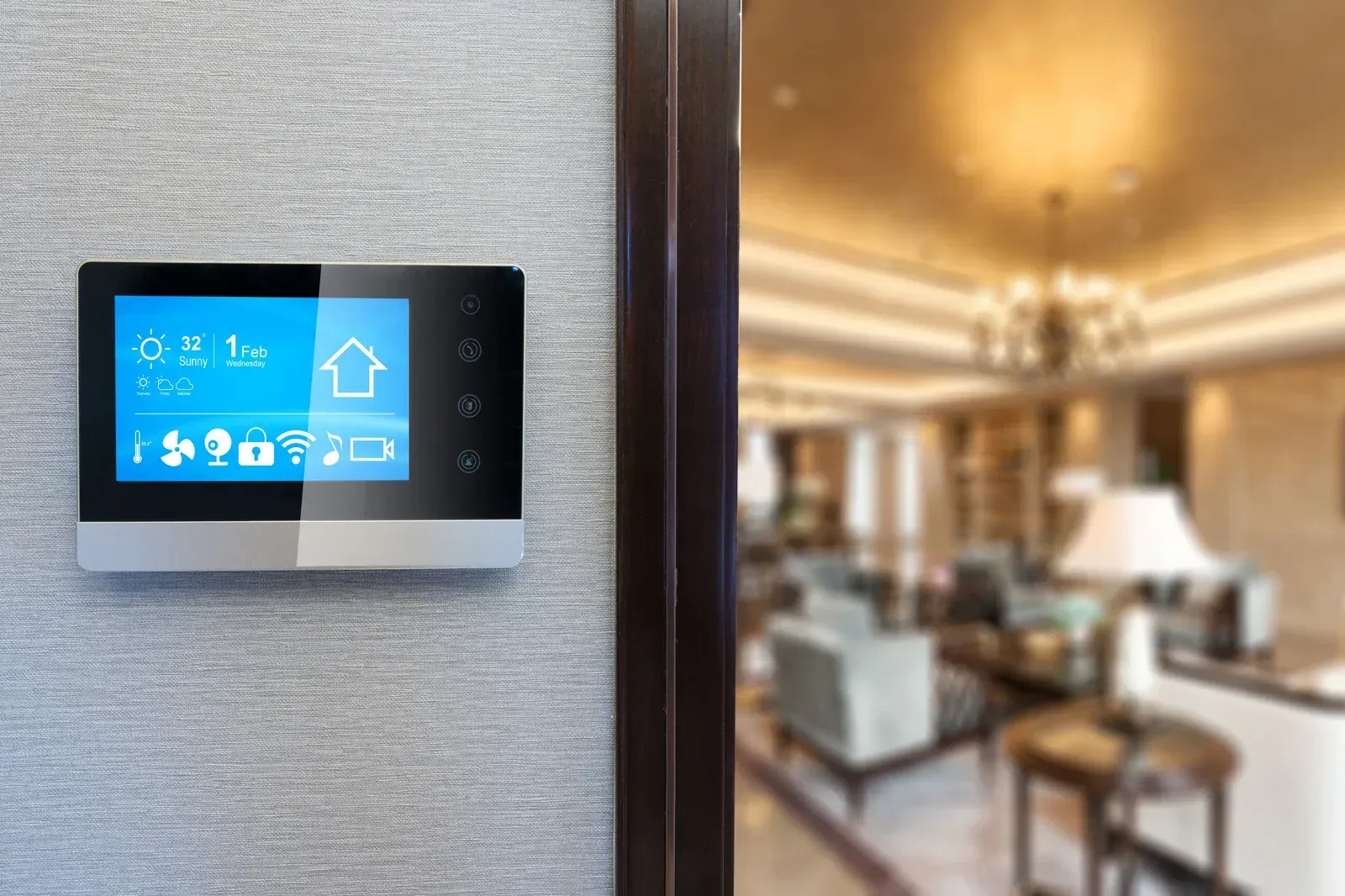 Smart home control panel on textured gray wall, with a blurred living room in the background.