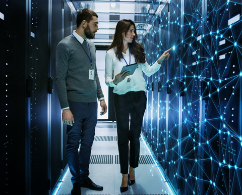 Female and Male IT Engineers Discussing Technical Details in a Working Data Center/ Server Room with Internet Connection Visualisation.