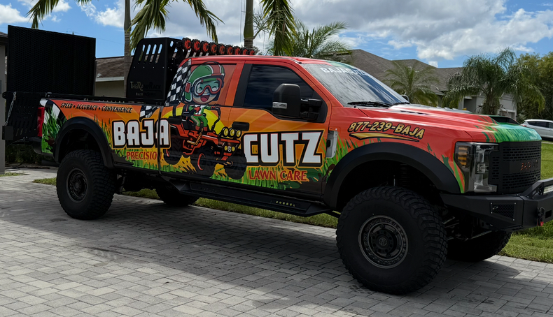 Garden bed filled with gravel and various shrubs. A bright orange pickup truck featuring a vibrant green and yellow