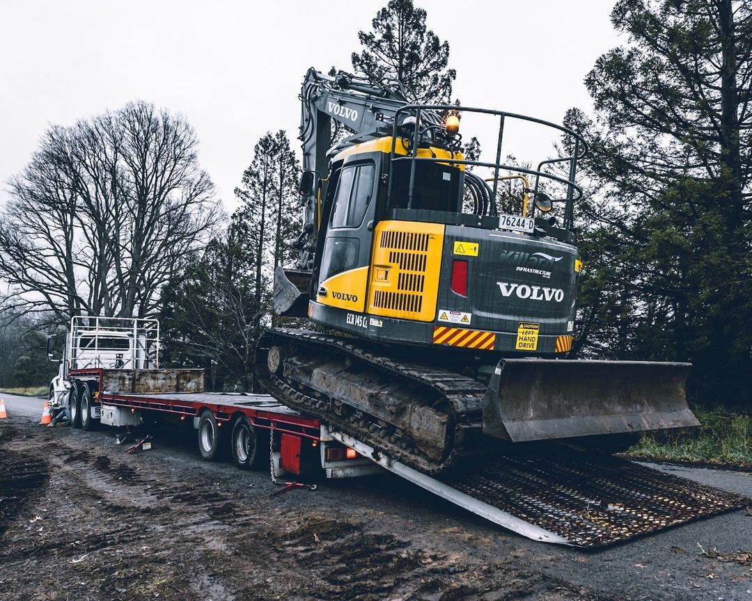 Excavator Loading onto A Flatbed Truck on A Muddy Road, Overcast Day — Highlands Water Cartage in Wagga Wagga, NSW