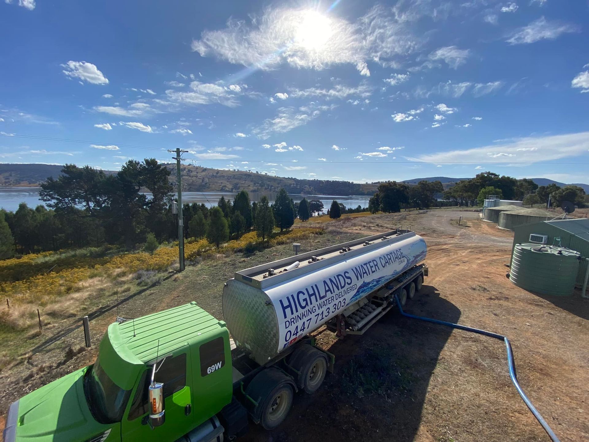 A Green Water Tanker Truck Filling up In a Rural Area. Cloudy Sky, Lake and Trees in The Background — Highlands Water Cartage in Wagga Wagga, NSW