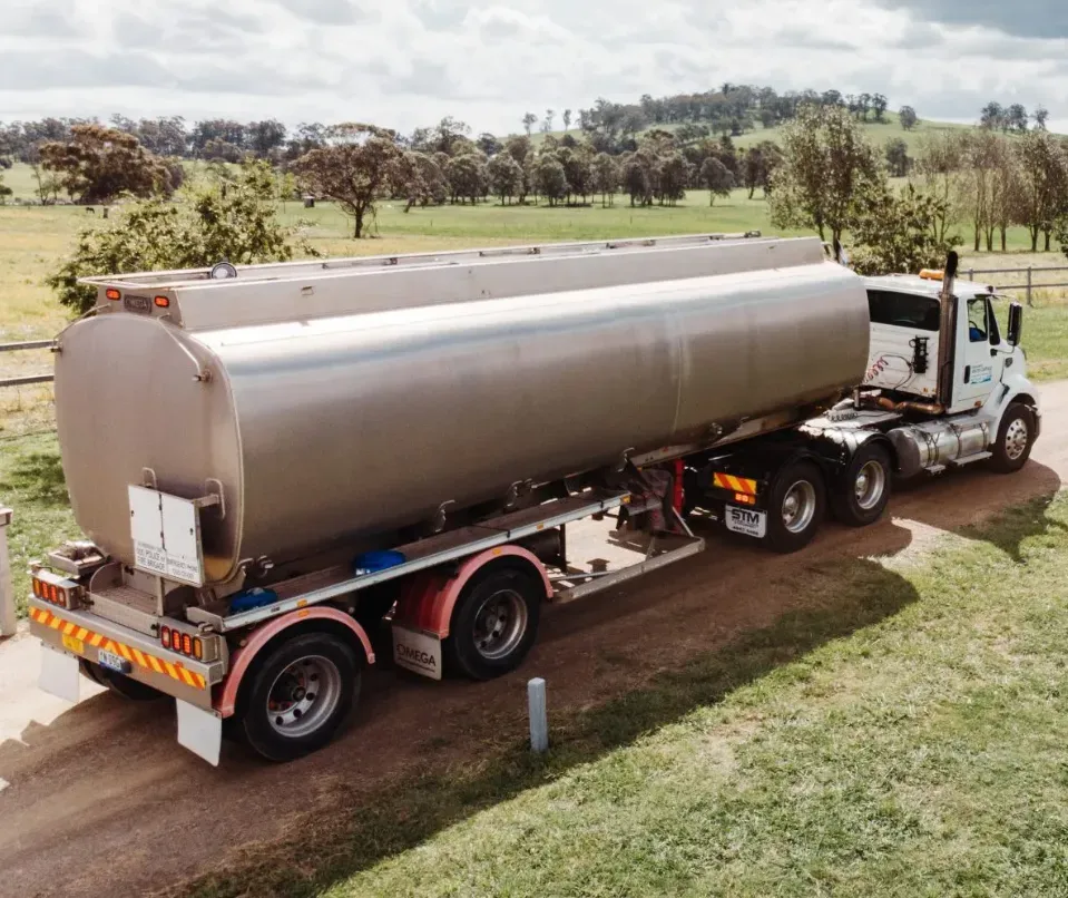 Silver tanker truck on a rural road, in front of a green field, trees, and buildings — Highlands Water Cartage in Glenquarry, NSW
