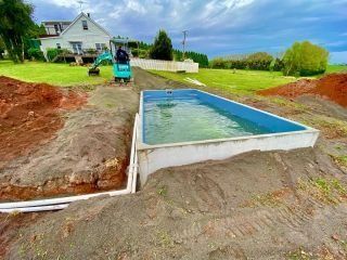 A rectangular pool sits in a construction site with dirt mounds, a small digger, and a house in the background — Highlands Water Cartage in Glenquarry, NSW