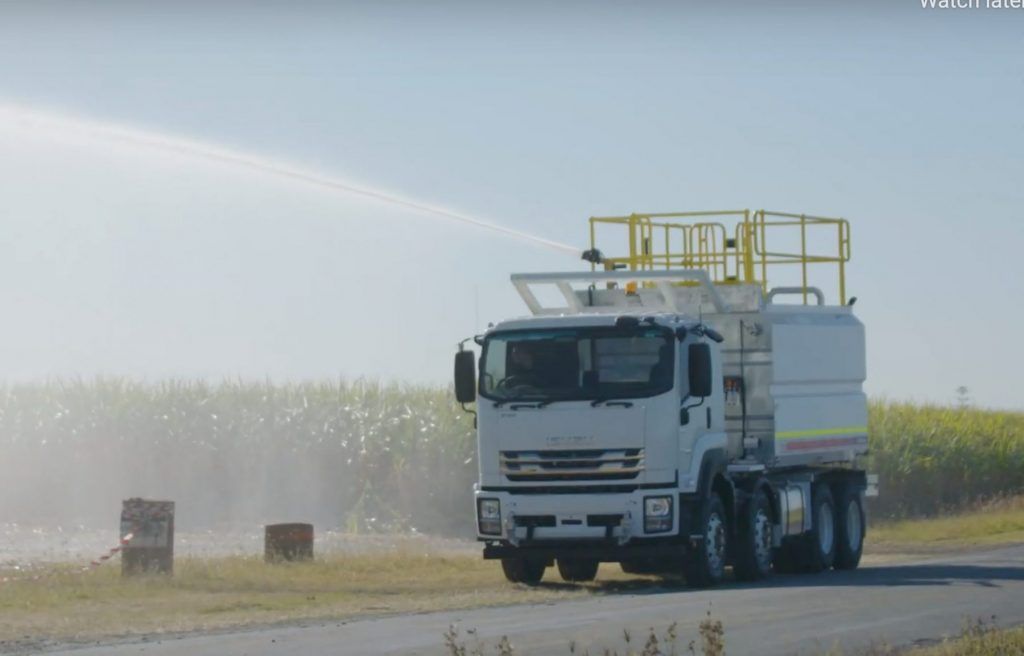 Water truck spraying water on a roadside field on a sunny day — Highlands Water Cartage in Glenquarry, NSW