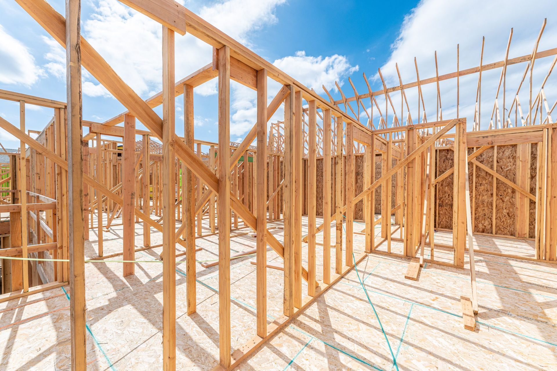 The wood-framed structure of a house under construction, featuring exposed wall studs and roof trusses against a blue sky.