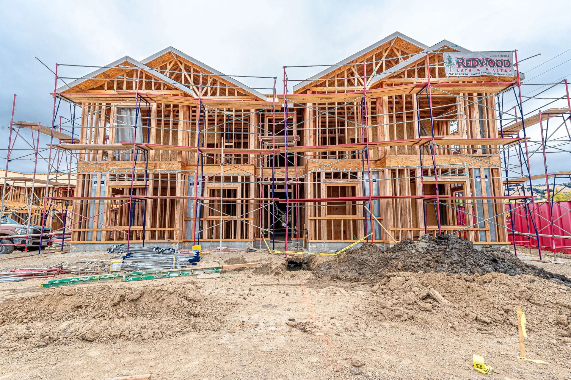 A large wooden frame of a two-story residential house under construction, surrounded by scaffolding and dirt.