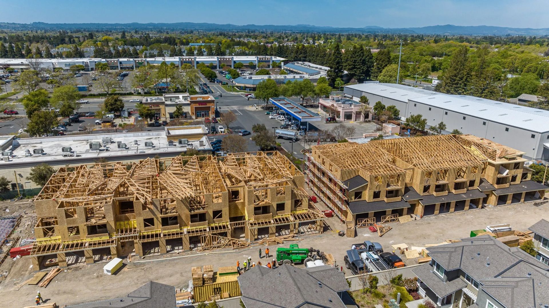 Aerial view of two wooden apartment building frames under construction in a suburban area.