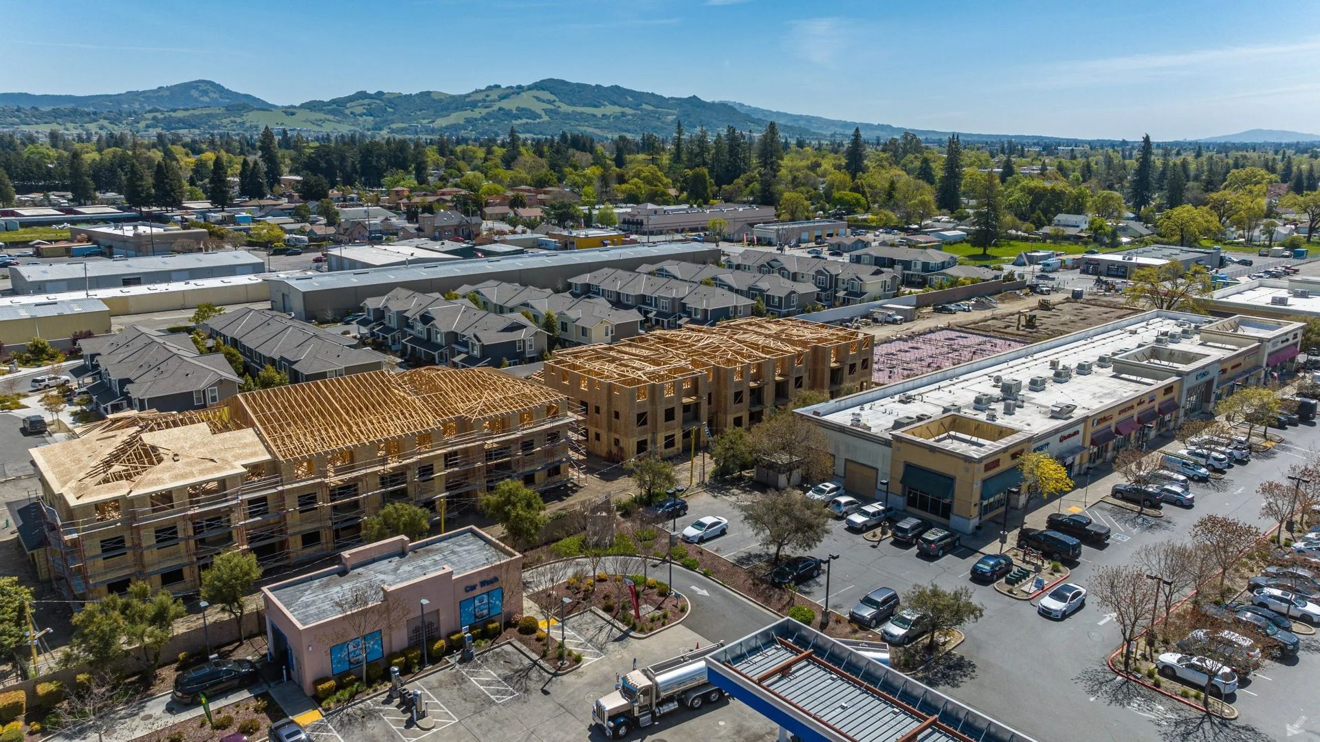 Aerial view of a residential construction site with wooden building frames, parking lots, and surrounding townhouses.