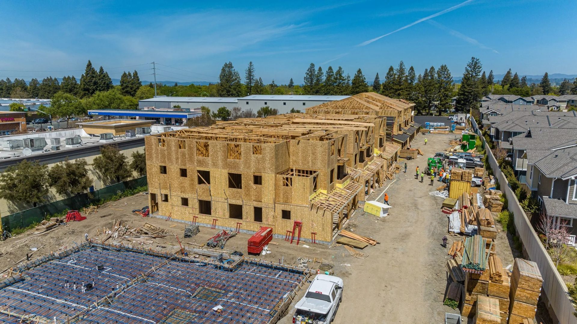 An aerial view of a wooden apartment building under construction, with a concrete foundation in the foreground.