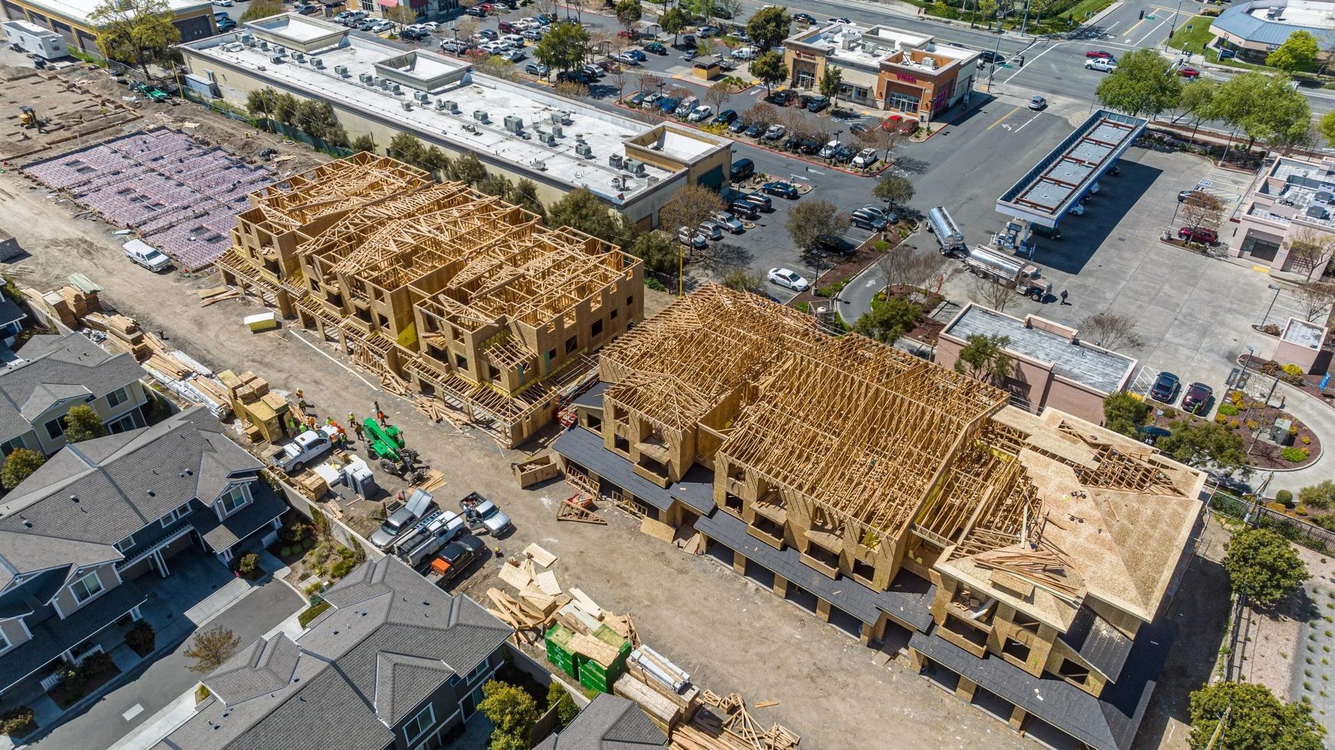 Aerial view of two residential apartment buildings under construction, surrounded by parking lots and suburban housing.