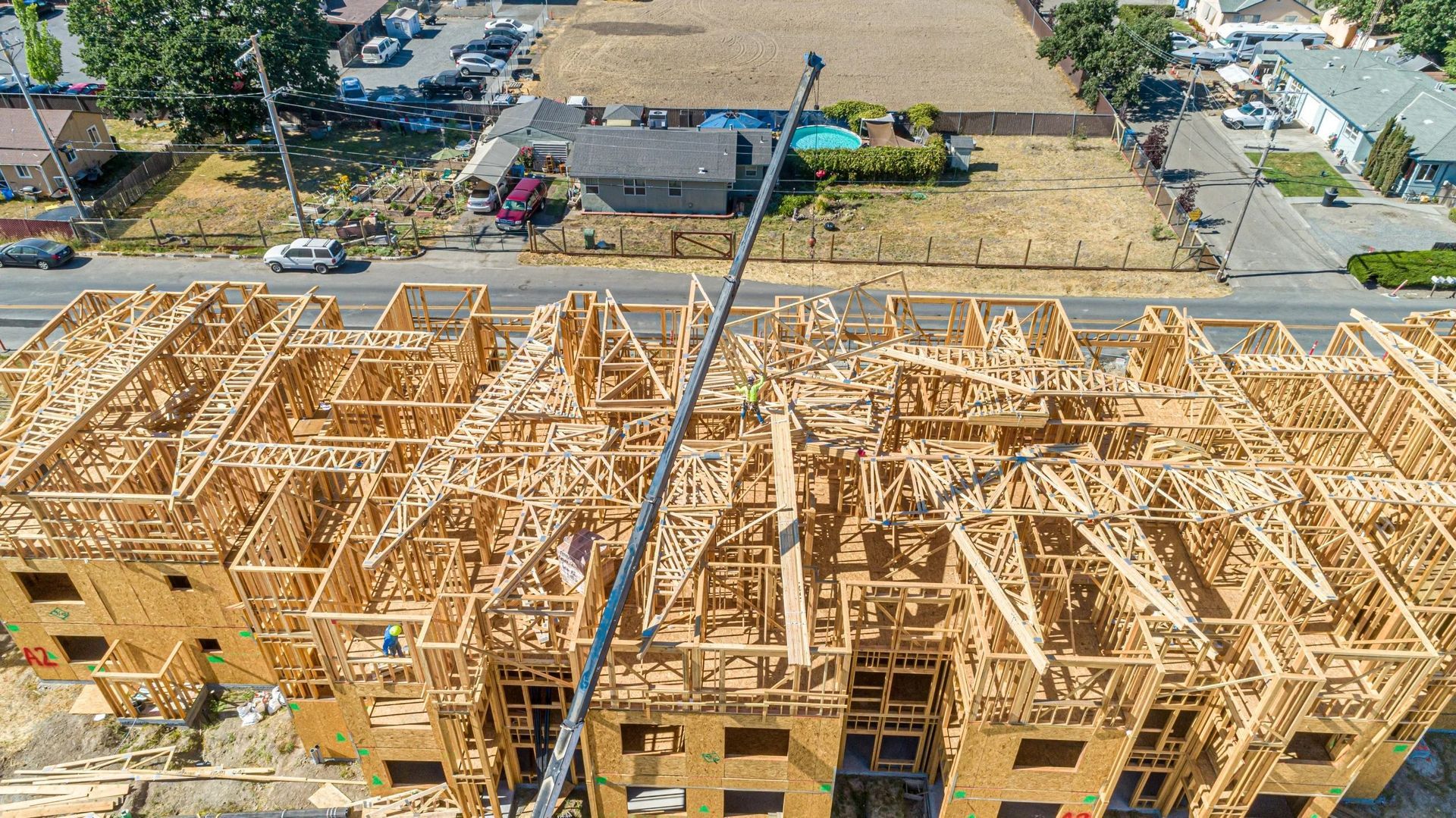 High-angle view of a large residential building under construction, showing a wooden frame structure and a crane boom.