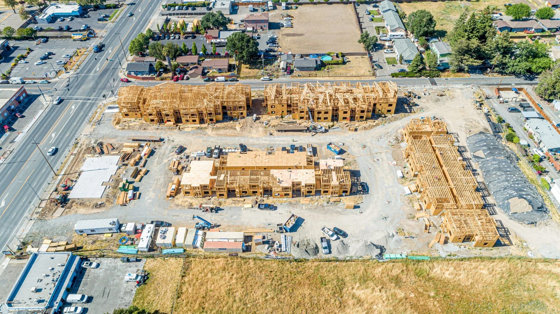 Aerial view of a residential construction site featuring wood-framed buildings in various stages of assembly.