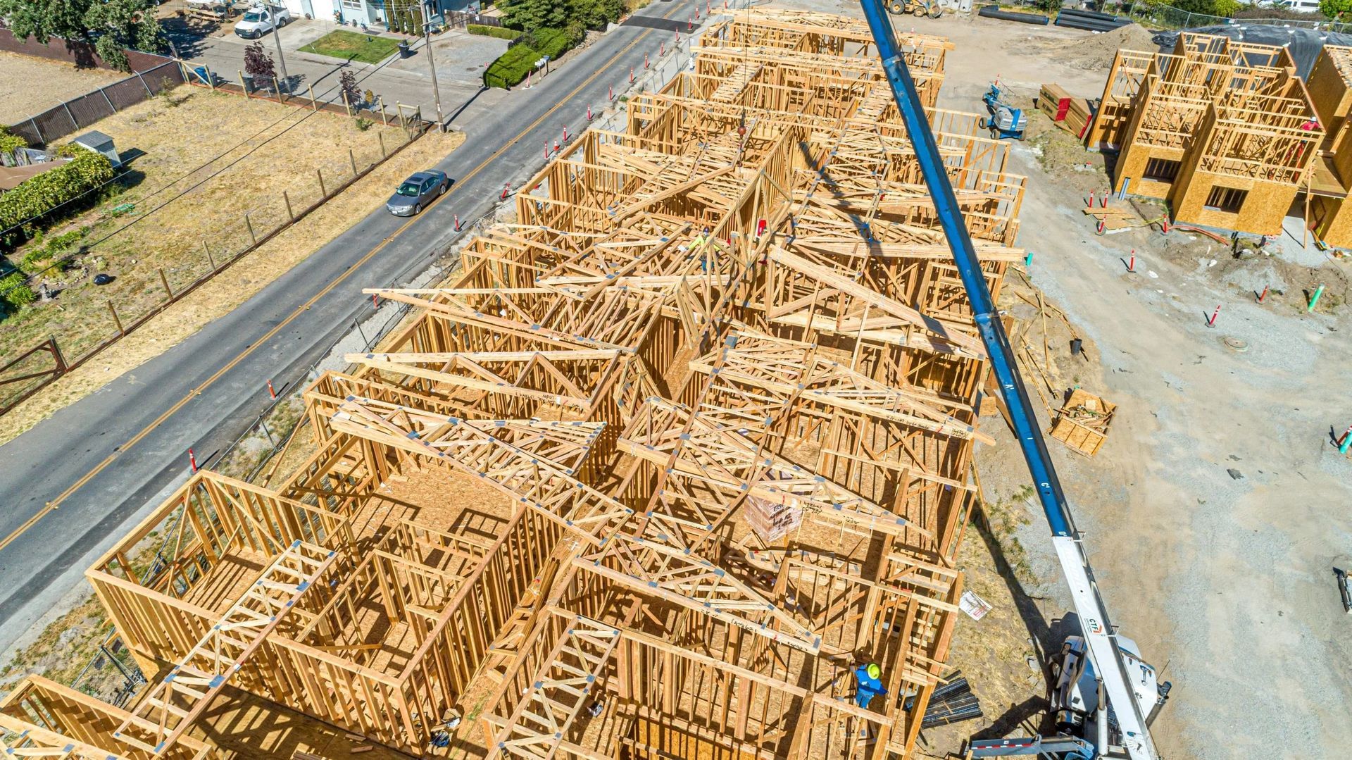 Aerial view of a residential construction site featuring wood-framed house skeletons and a large crane.