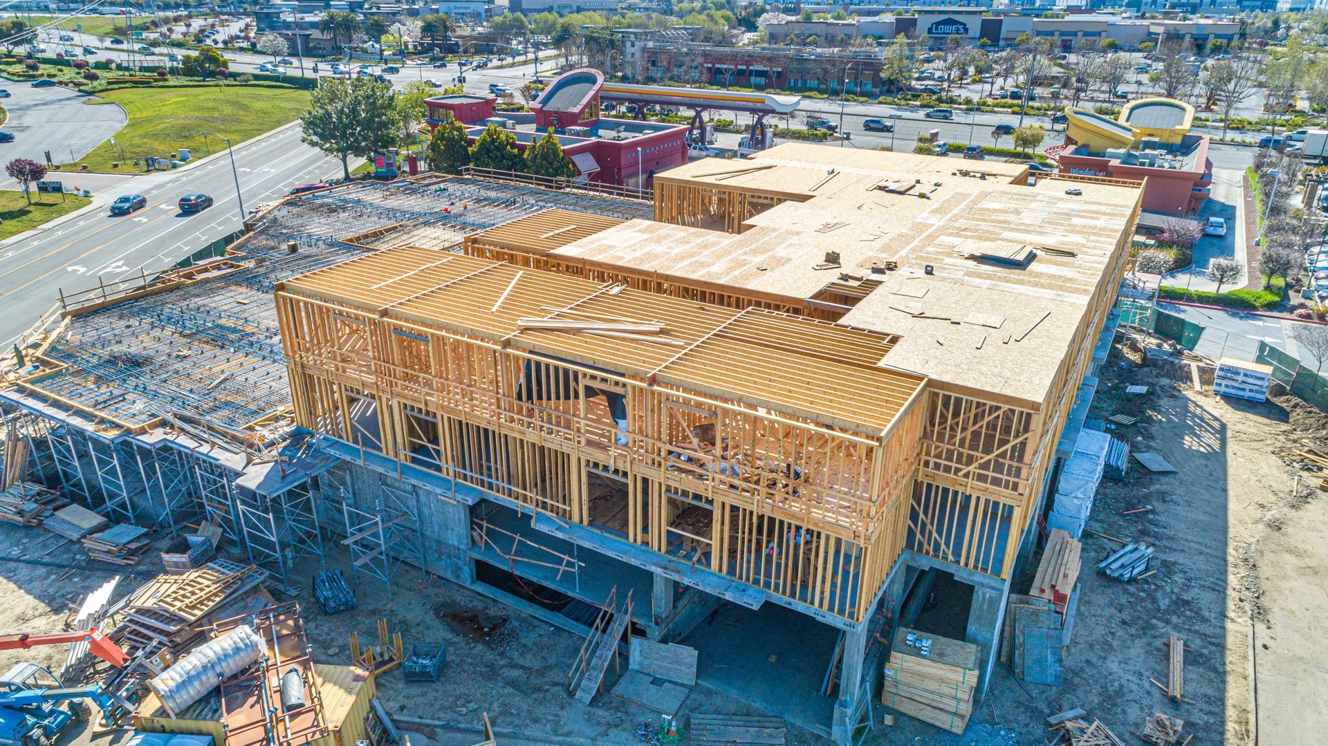 An aerial view of a multi-story commercial building under construction with exposed wooden framing and plywood roof.