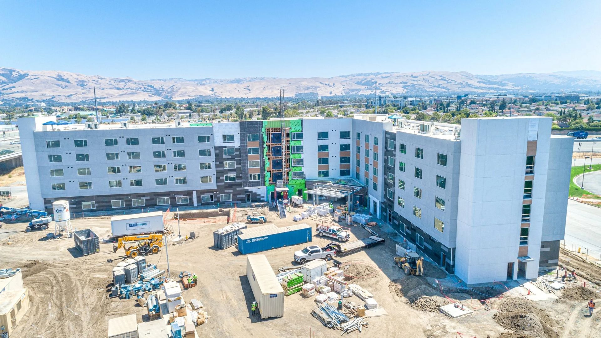 An aerial view of a multi-story hotel under construction, surrounded by building materials and heavy machinery.