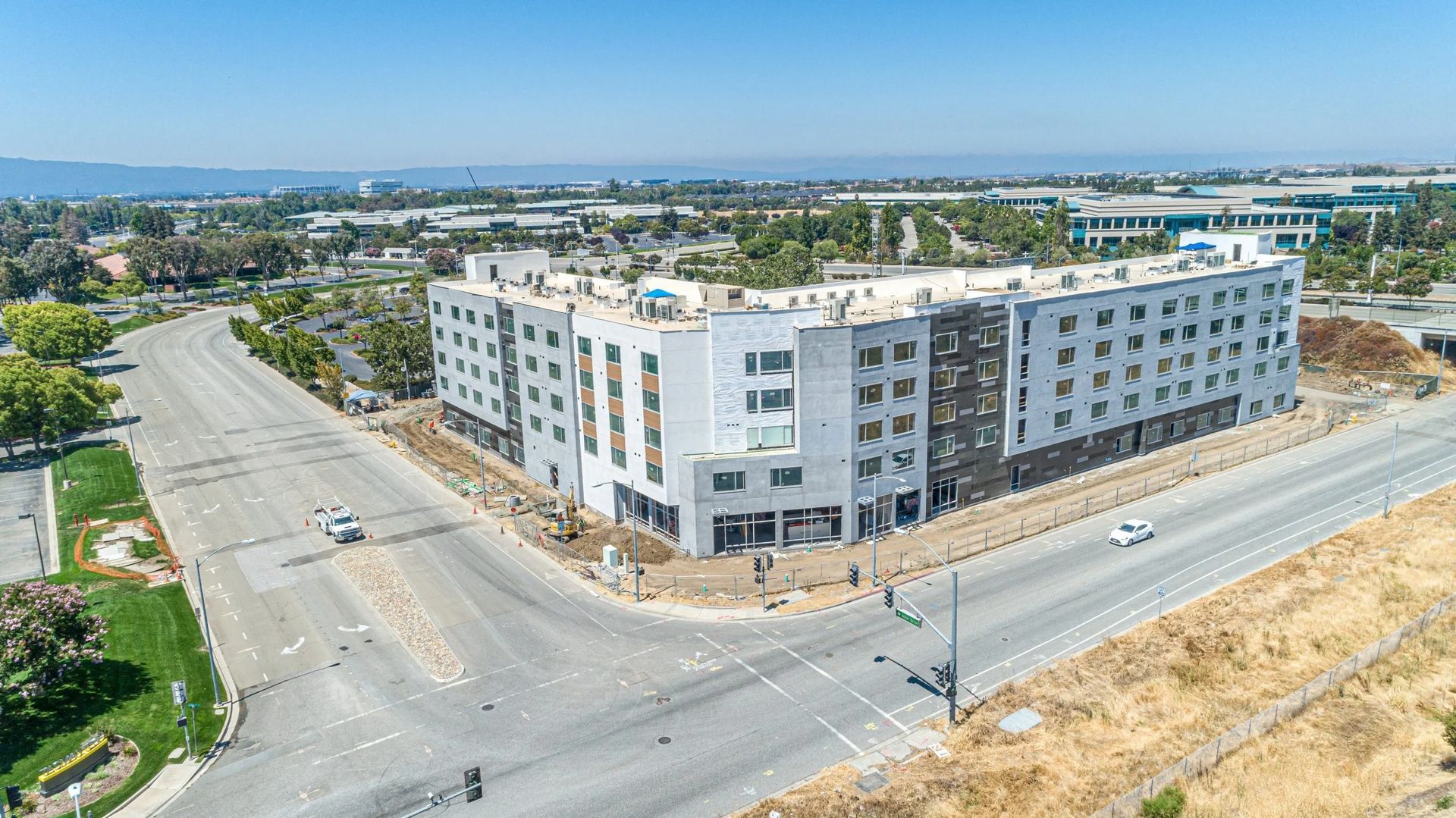 An aerial view of a multi-story, modern apartment building under construction on a sunny day at a street intersection.