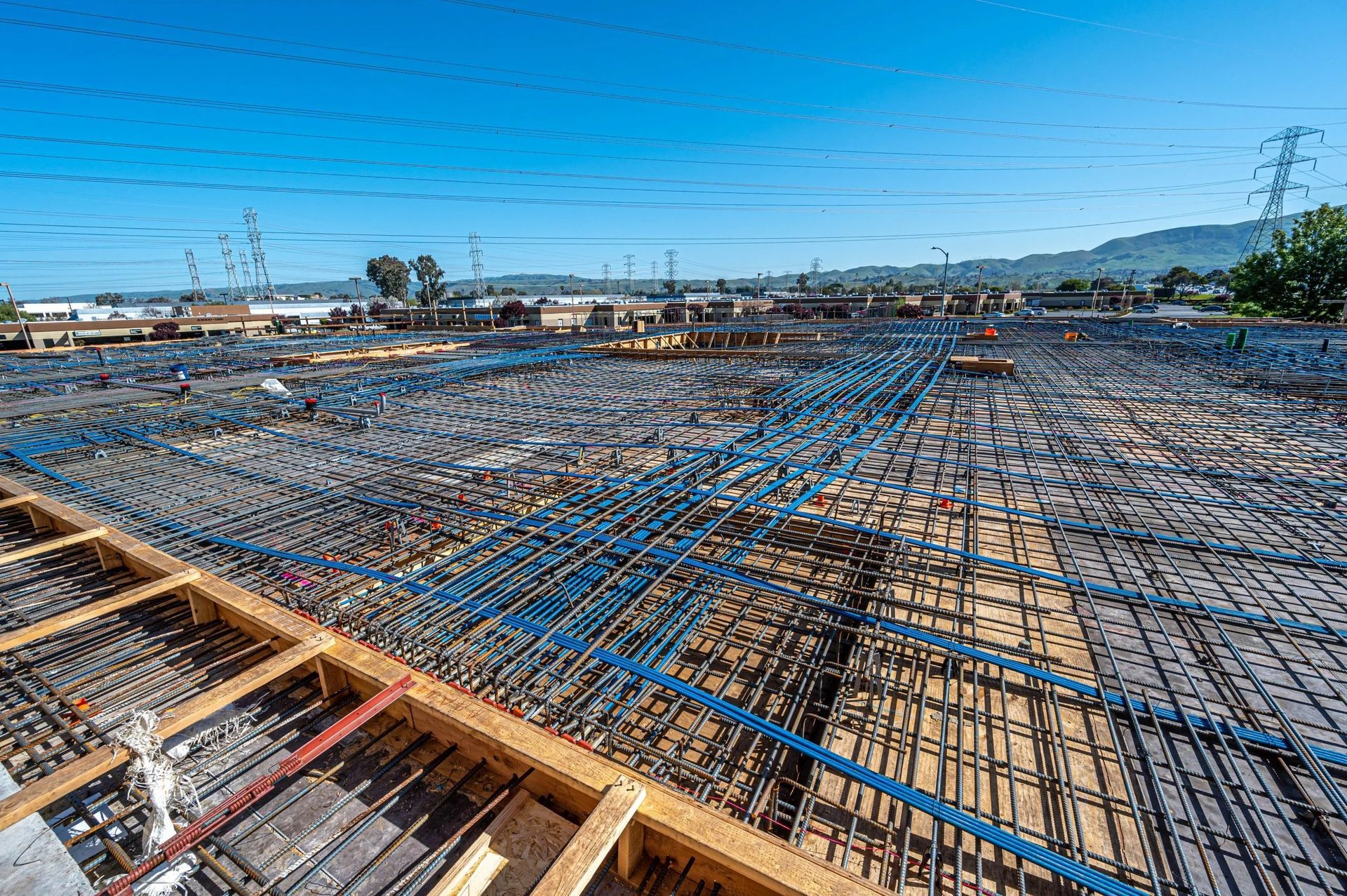 A vast construction site with a grid of steel rebar reinforcement and wooden framework against a clear blue sky.