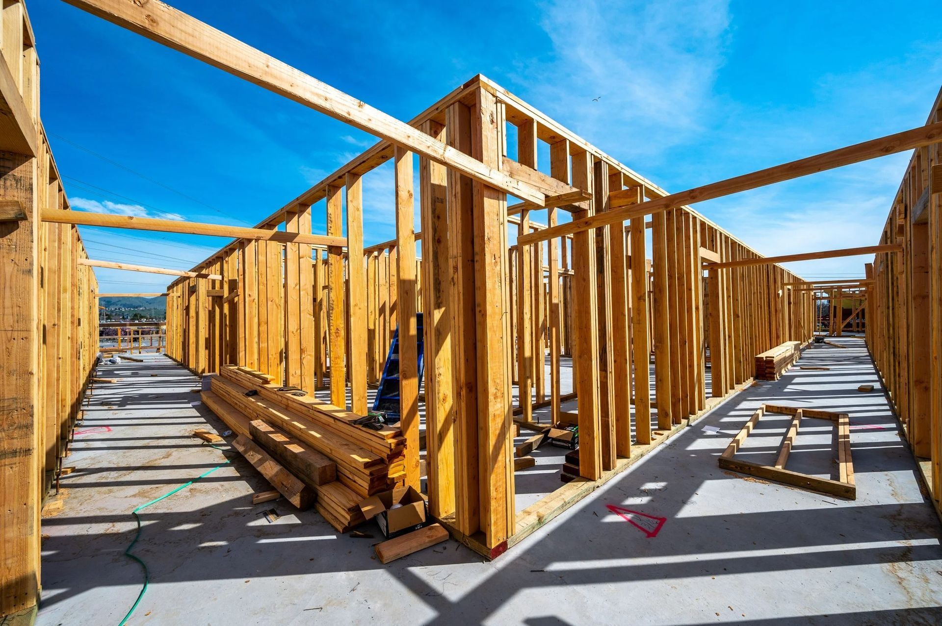 Wooden framing of a new building under construction, showing wall studs and support beams under a bright blue sky.
