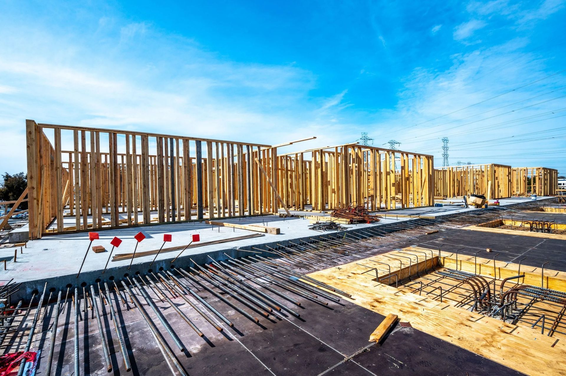 The wooden framework of a building under construction, featuring exposed rebar on a concrete foundation under a blue sky.