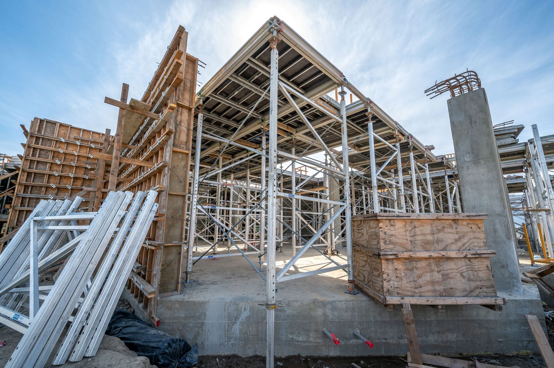 Construction site with steel framing, wooden formwork, and stacks of white beams under a clear sky