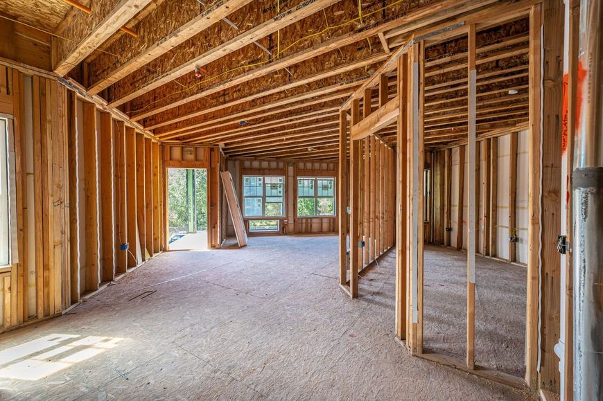 The interior of a house under construction with exposed wooden wall studs, ceiling joists, and subflooring.