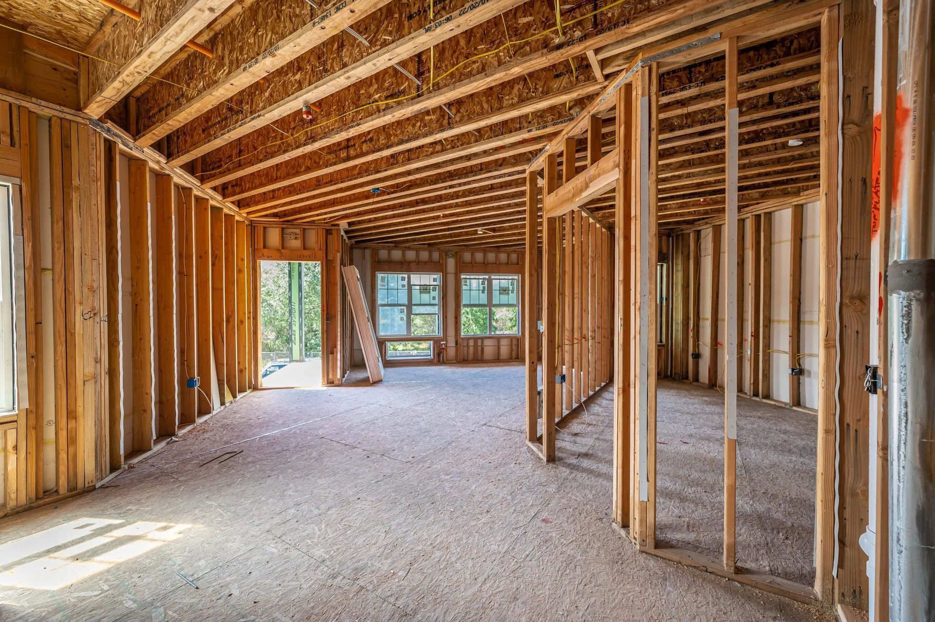 Interior view of a residential building under construction with exposed wooden wall studs and ceiling joists.