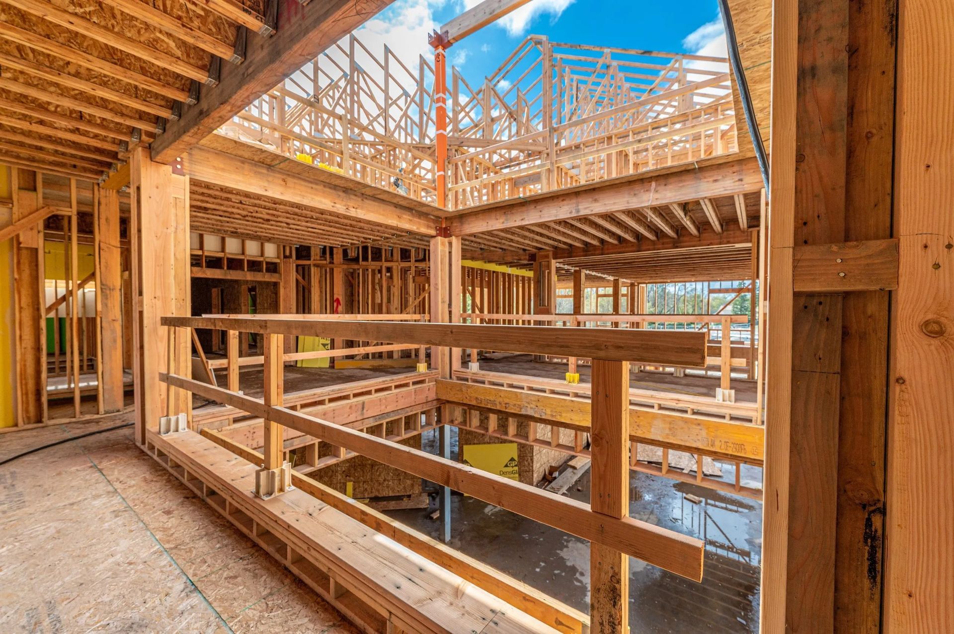 The interior of a building under construction featuring exposed wood framing, floor joists, and a safety railing.