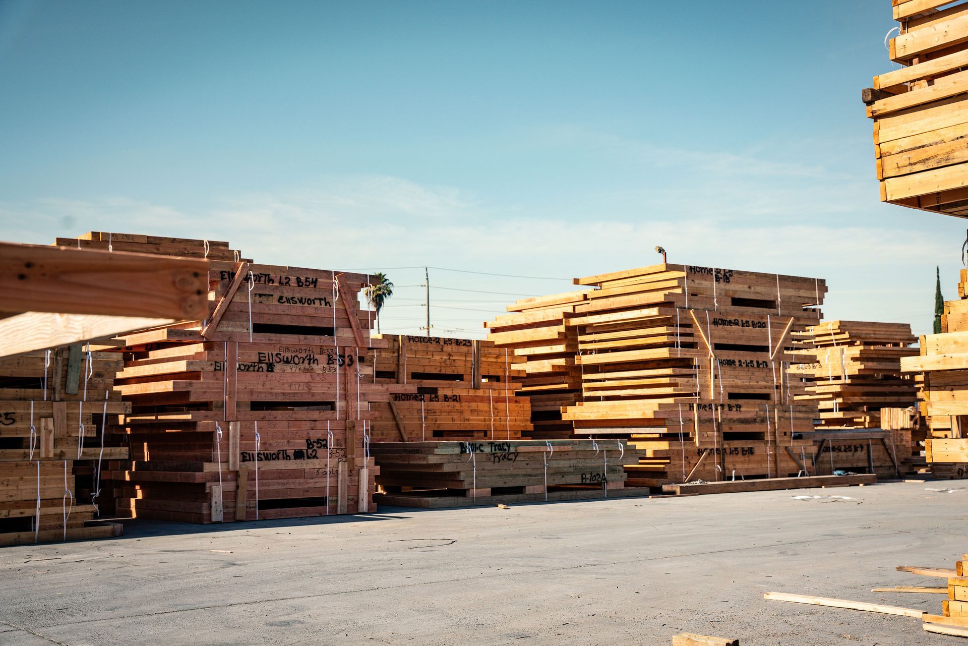 Stacks of cut lumber stacked in an outdoor lumber yard under a clear blue sky
