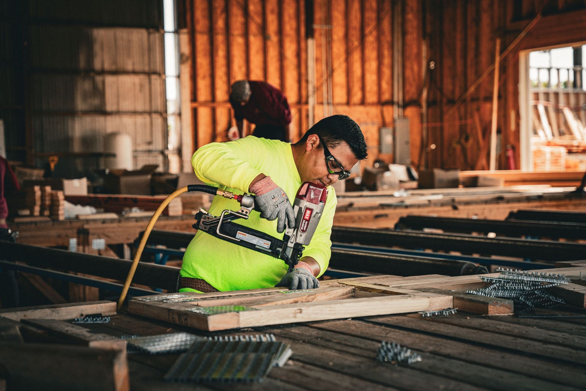 Worker in neon safety gear cutting wood at a construction site with sparks flying
