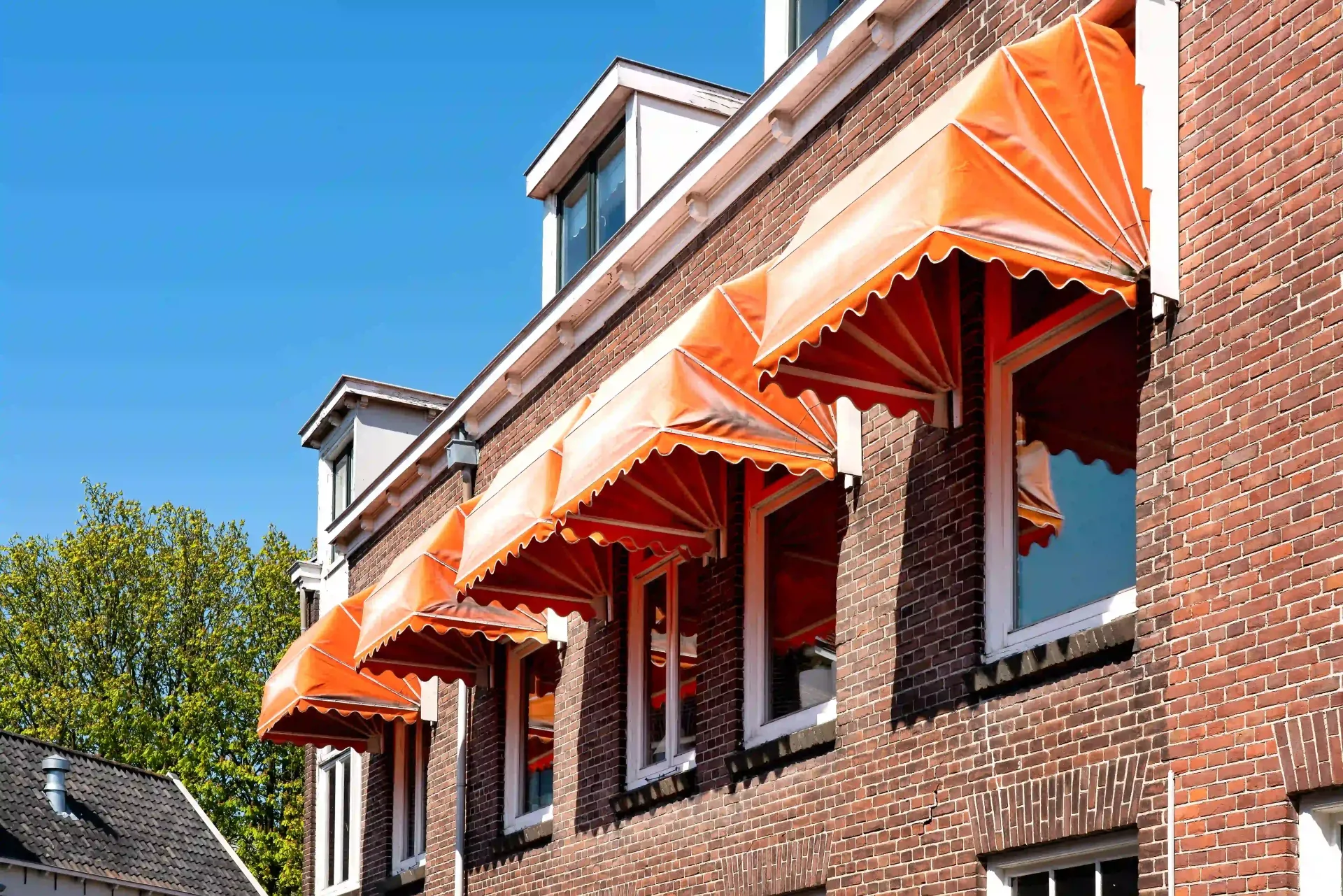 A row of orange European fabric awnings providing shade on a red brick building.
