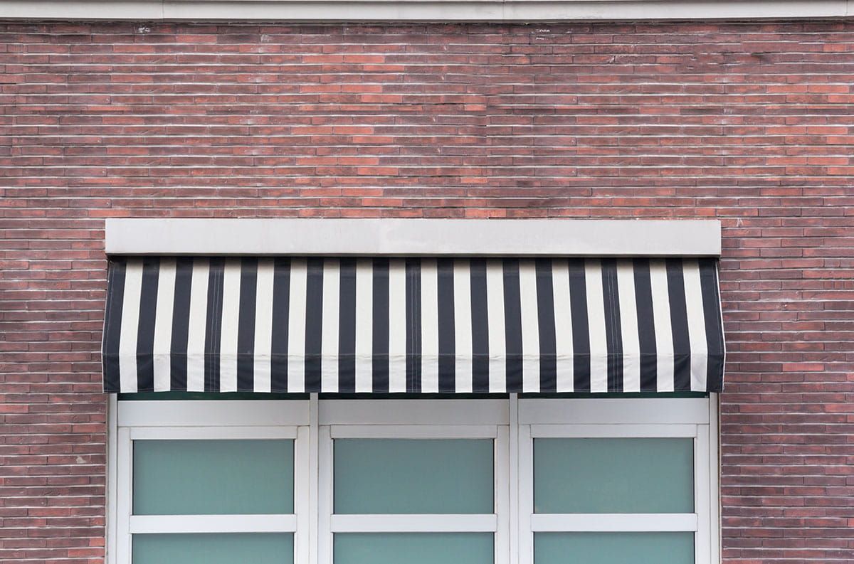 A retractable black and white striped house awning design installed above three windows on a brick b