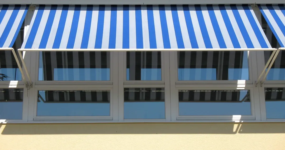 Blue and white striped manual retractable awning extended to provide shade over a row of building wi