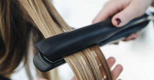 A woman is getting her hair straightened with a flat iron.