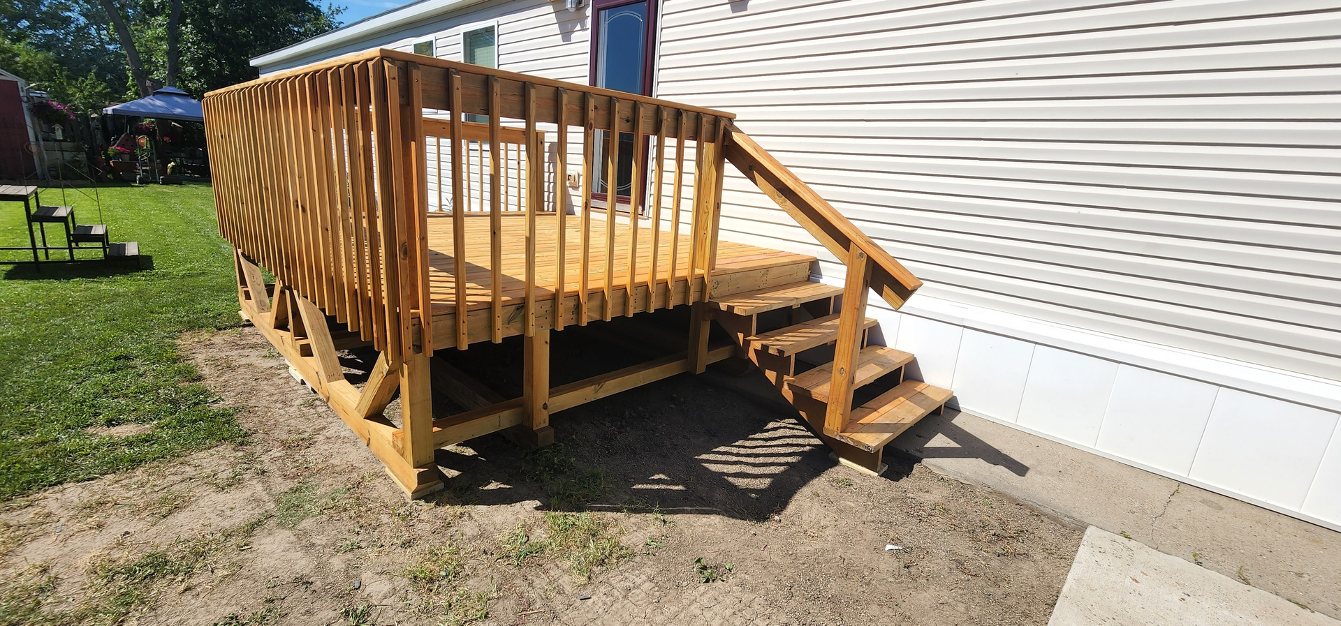 A newly constructed wooden deck with railings and steps attached to the side of a mobile home.
