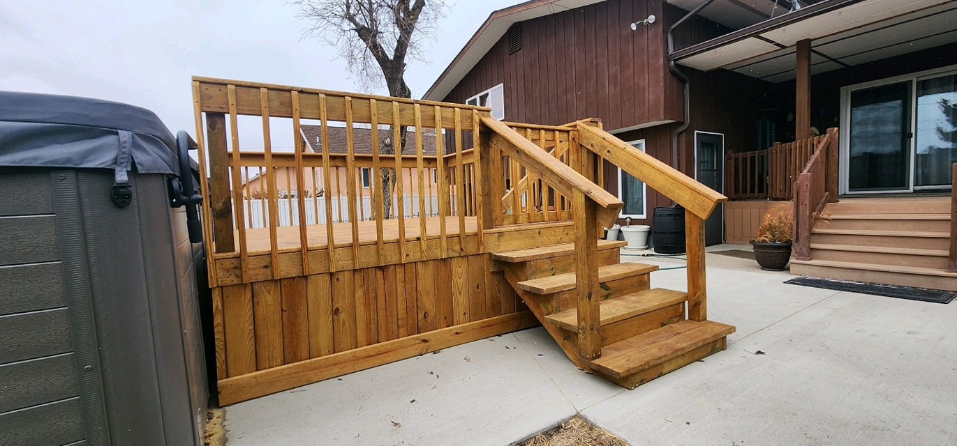 A newly built, stained wooden deck with stairs, a railing, and surrounding lattice skirting on a concrete patio.