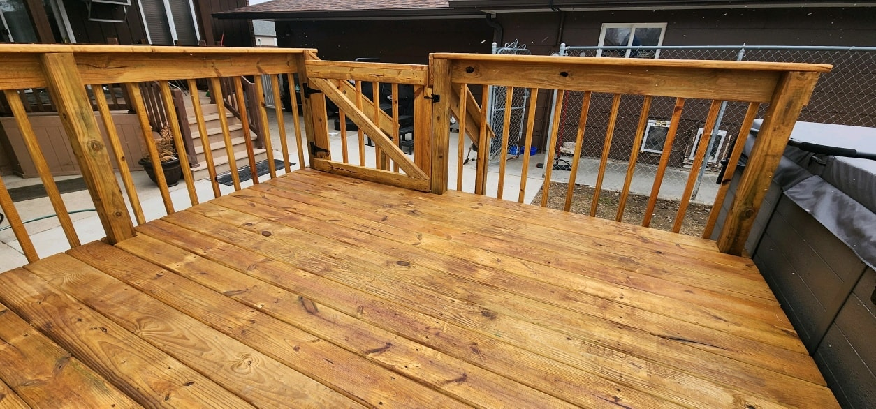 A wide-angle view of a freshly stained, honey-colored wooden deck with matching railings and a small gate.
