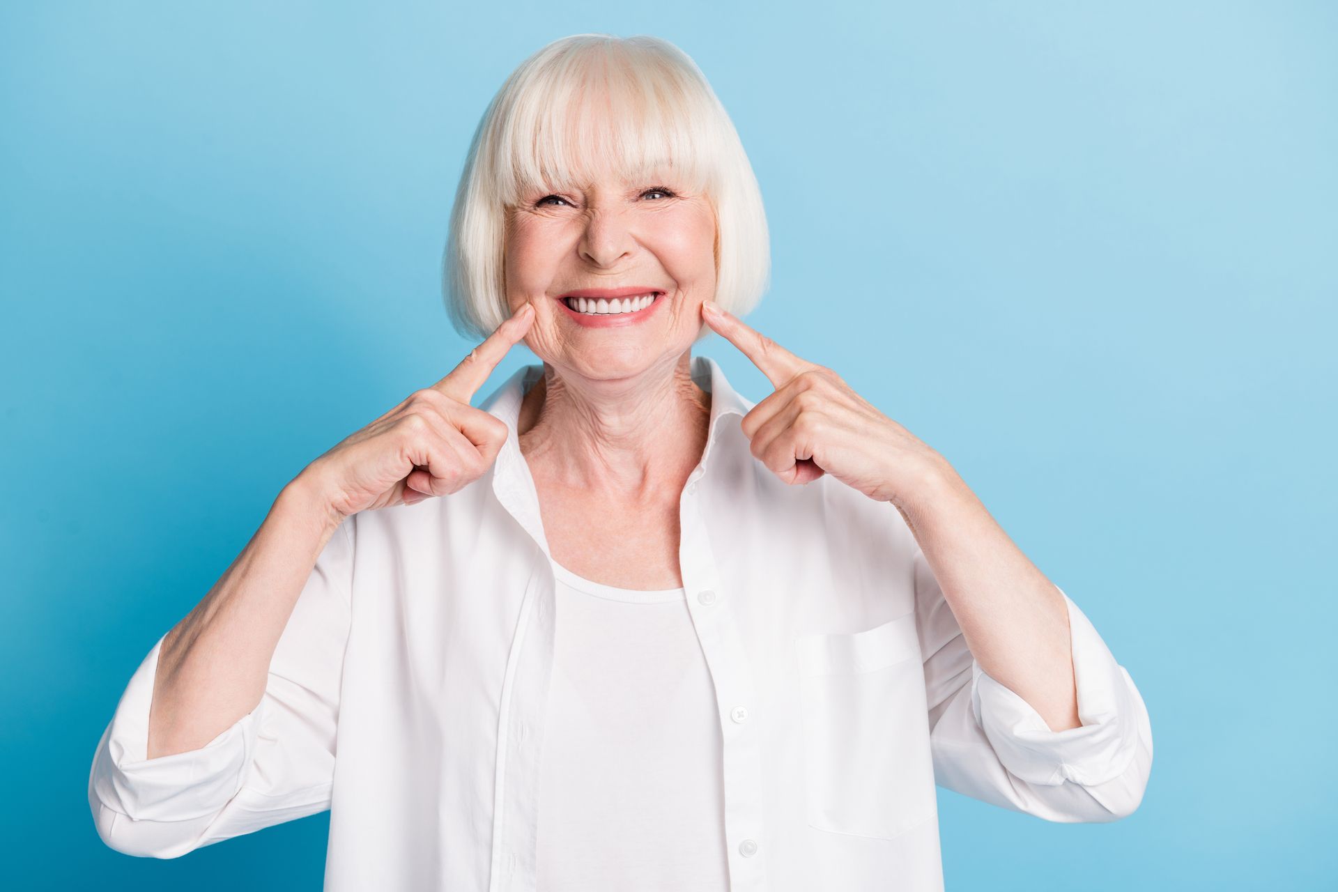 Portrait of a senior woman pointing at her white, healthy smile, showcasing local denture services.