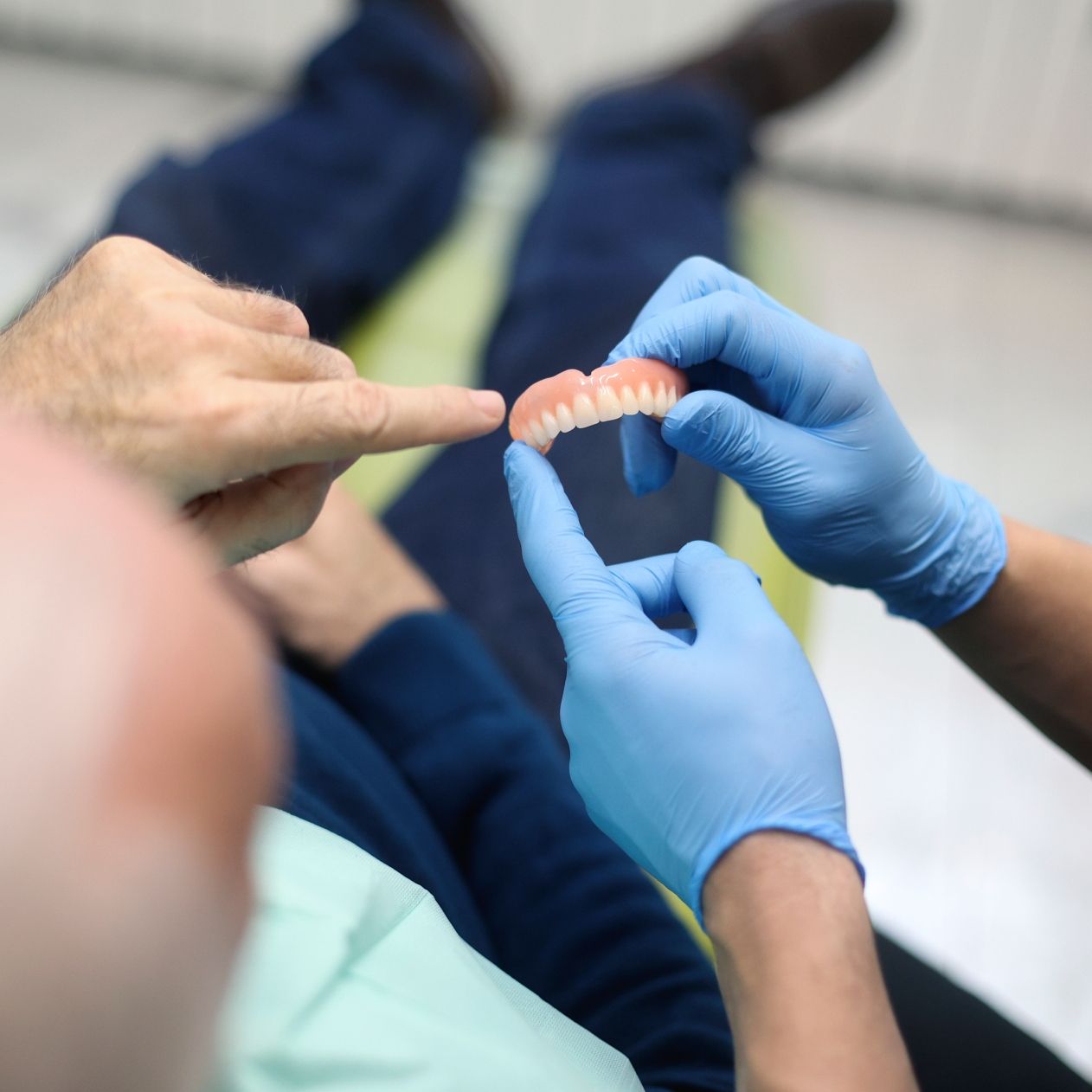 Dental Clinic — Port Noarlunga, SA — Natural Denture Clinic A person points at dentures held by gloved hands, likely discussing the fit.