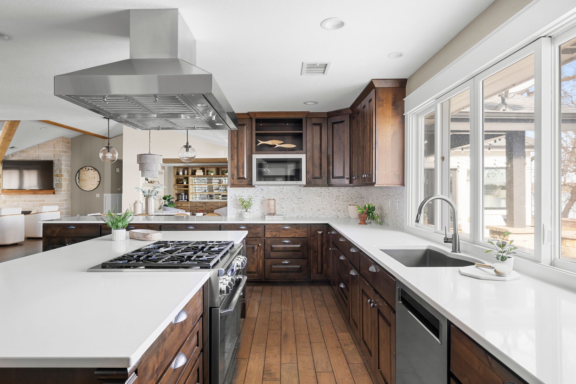 Modern kitchen with dark wood cabinets, white countertops, stainless steel appliances, and large windows.