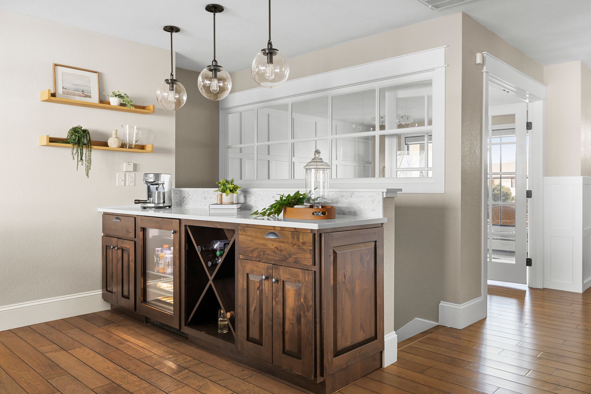 A home bar with dark wooden cabinets, white countertop, wine rack, and hanging lights; wooden floors.